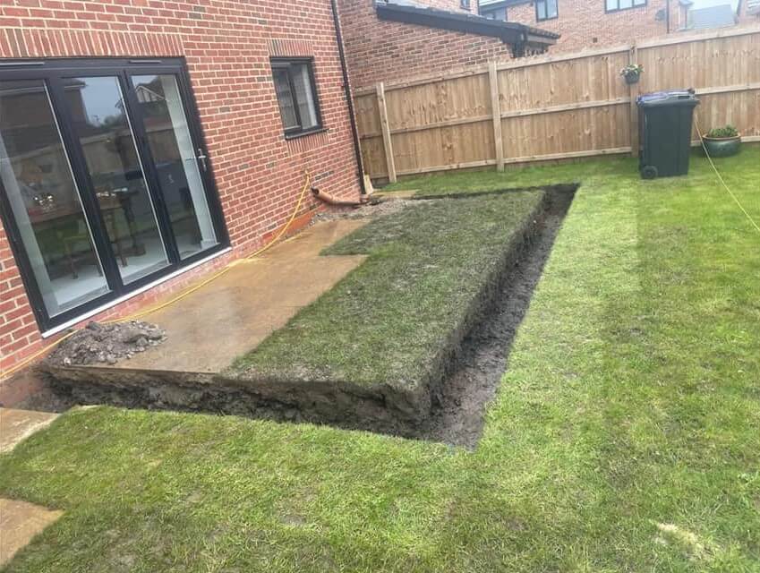 A backyard with a small patio and a lawn, showing the beginning of a house extension in the garden.