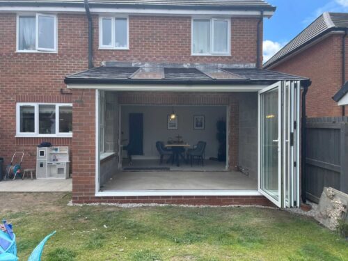 Rear home extension on a brick house featuring large, bi-fold glass doors that open up to a spacious new interior
