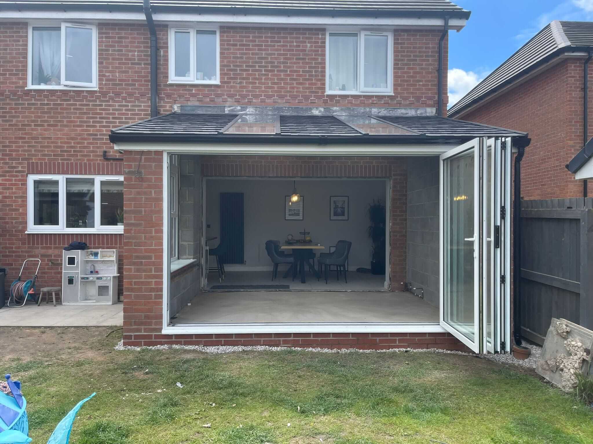 Rear home extension on a brick house featuring large, bi-fold glass doors that open up to a spacious new interior