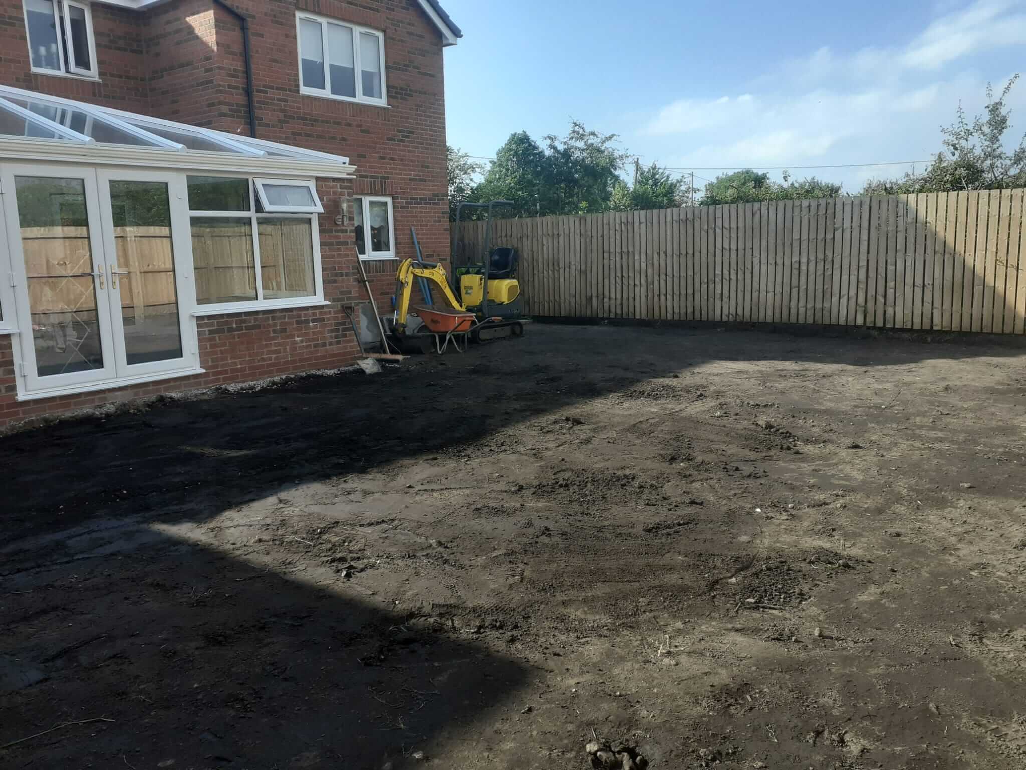 A backyard undergoing renovation with exposed soil and construction equipment.