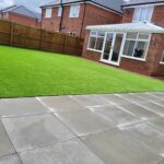 A newly renovated backyard featuring a lush green artificial lawn and a clean, neatly laid concrete patio.