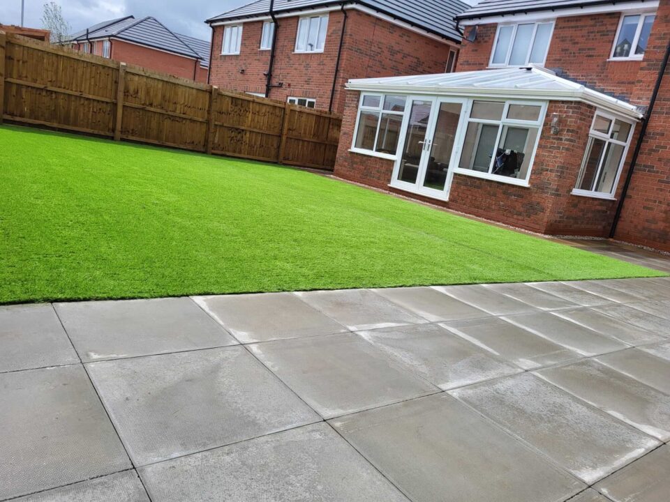 A newly renovated backyard featuring a lush green artificial lawn and a clean, neatly laid concrete patio.